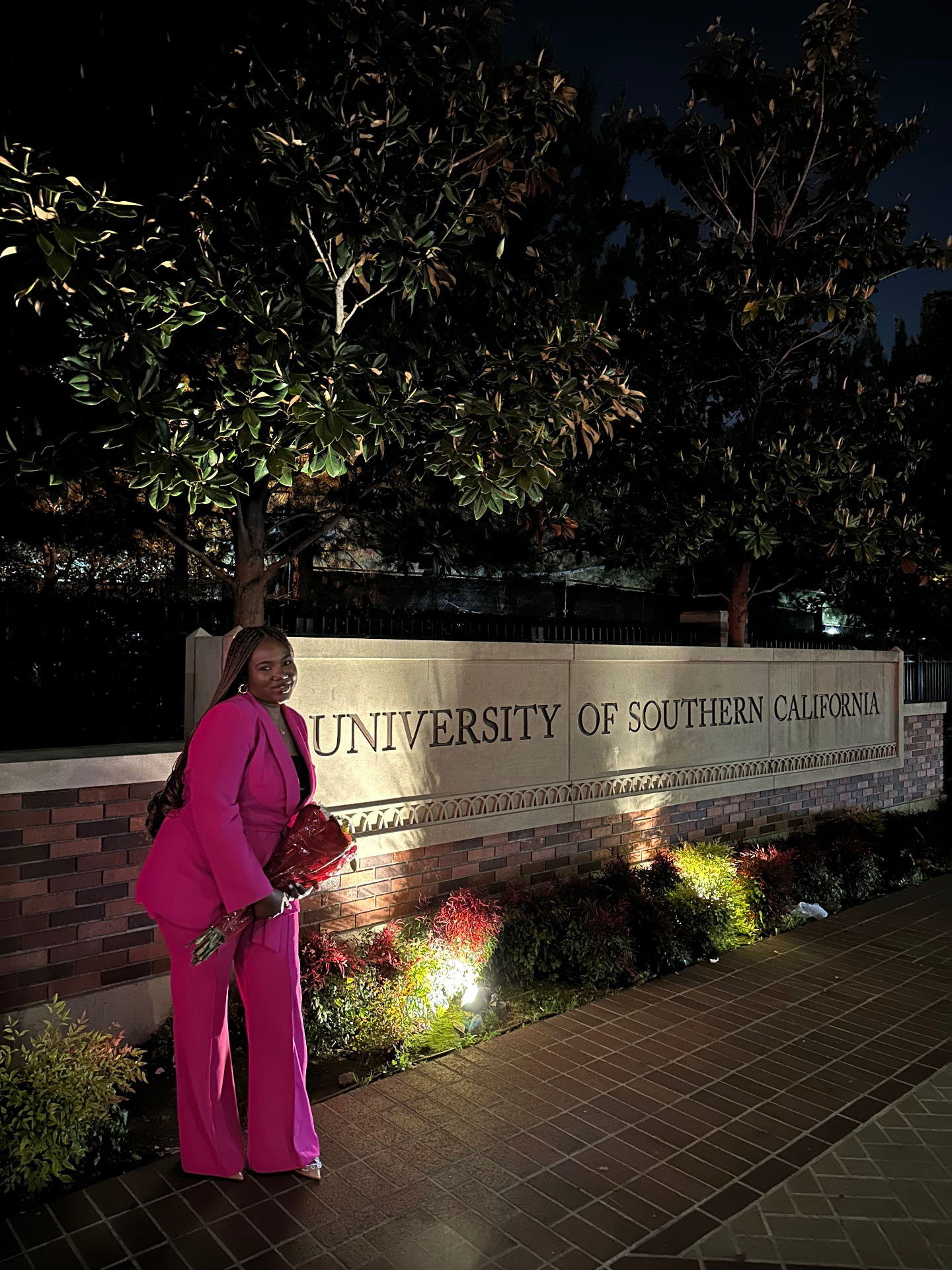 Oluseun in a pink suit standing by the University of Southern California sign at night